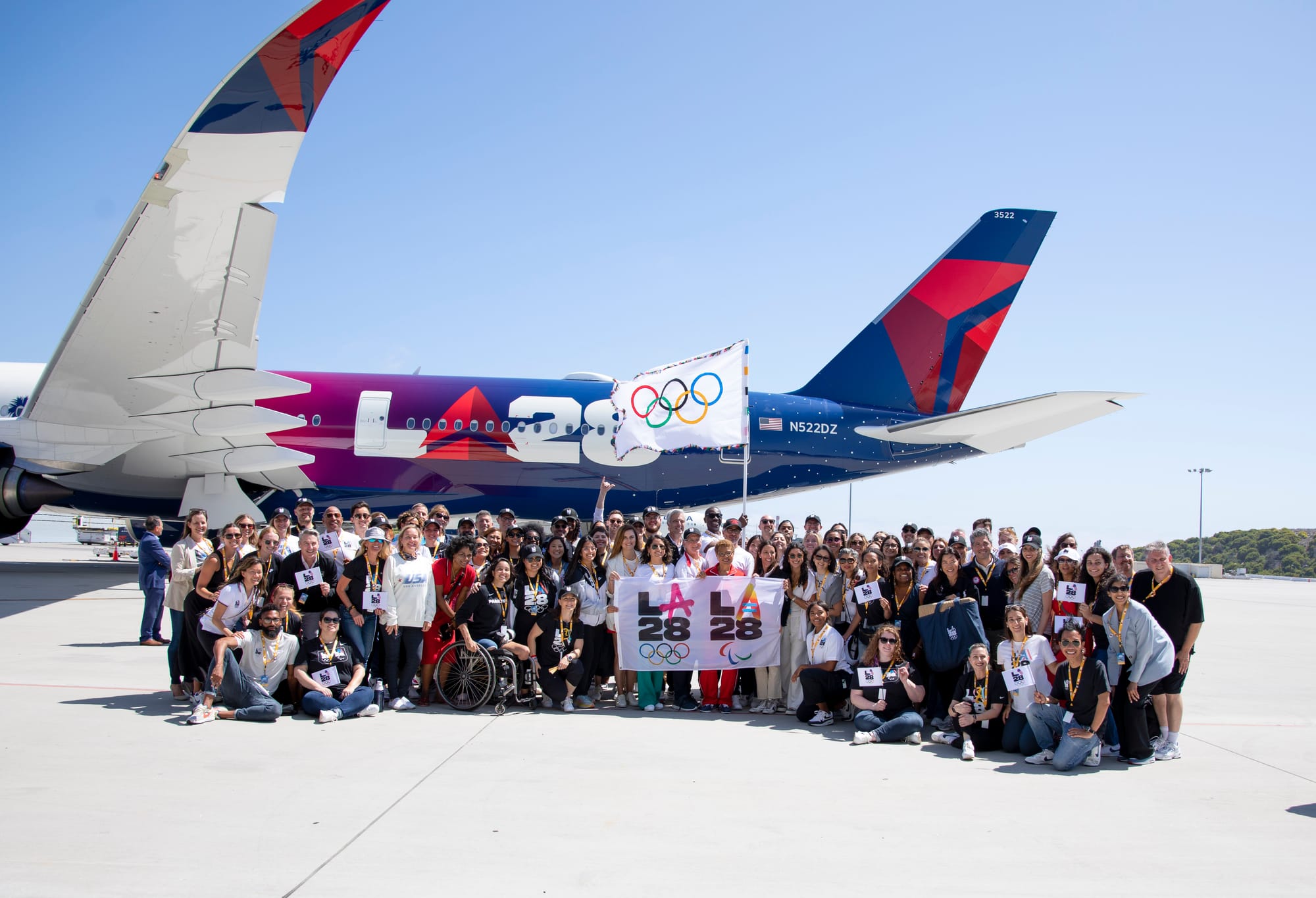 A large crowd of people, including LA Mayor Karen Bass, standing in front of an LA28 branded Delta plane on the tarmac at LAX