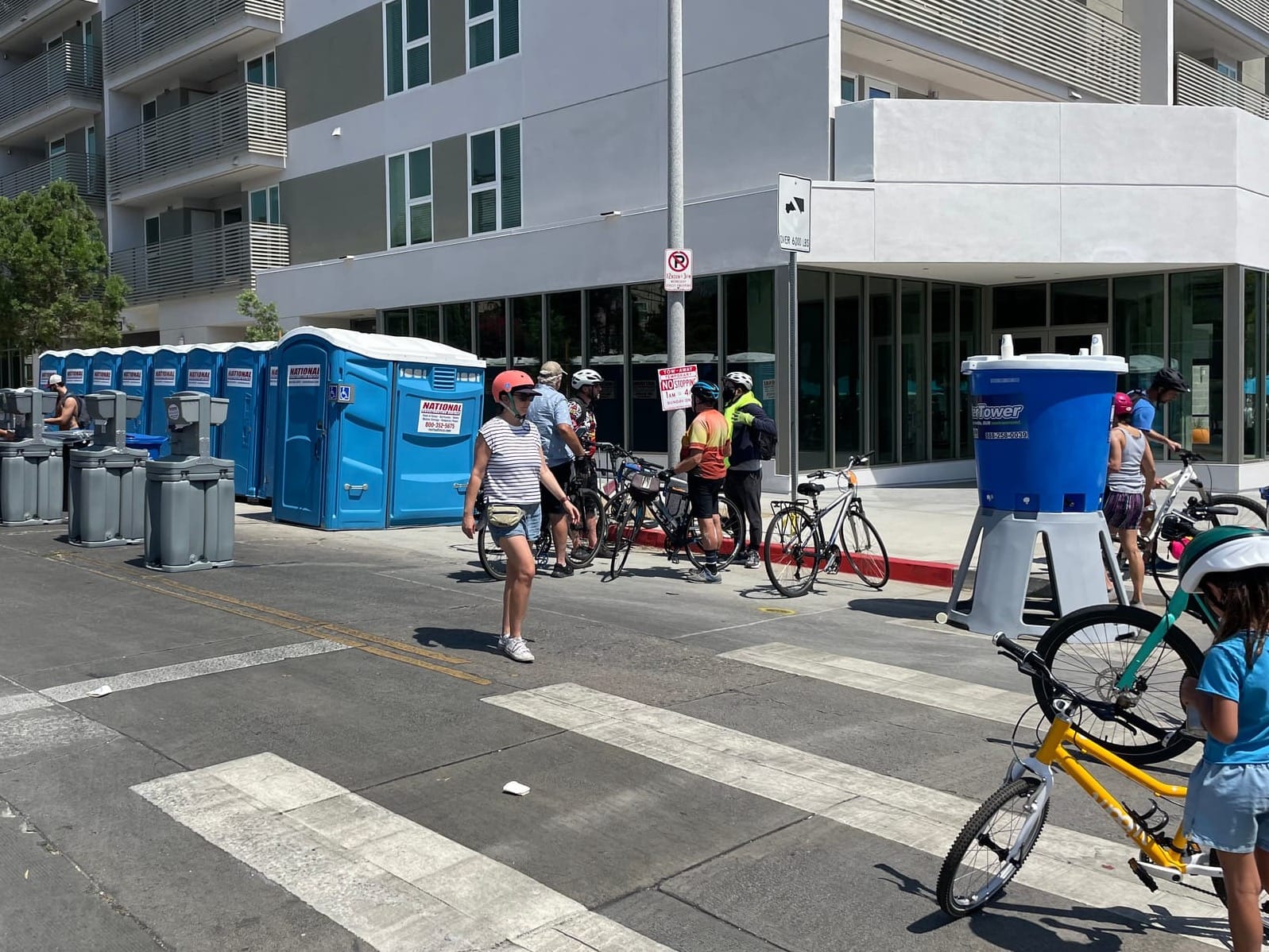 Portable bathrooms and a water tower are lined up along a closed street at CicLAvia where people on bikes are taking a break