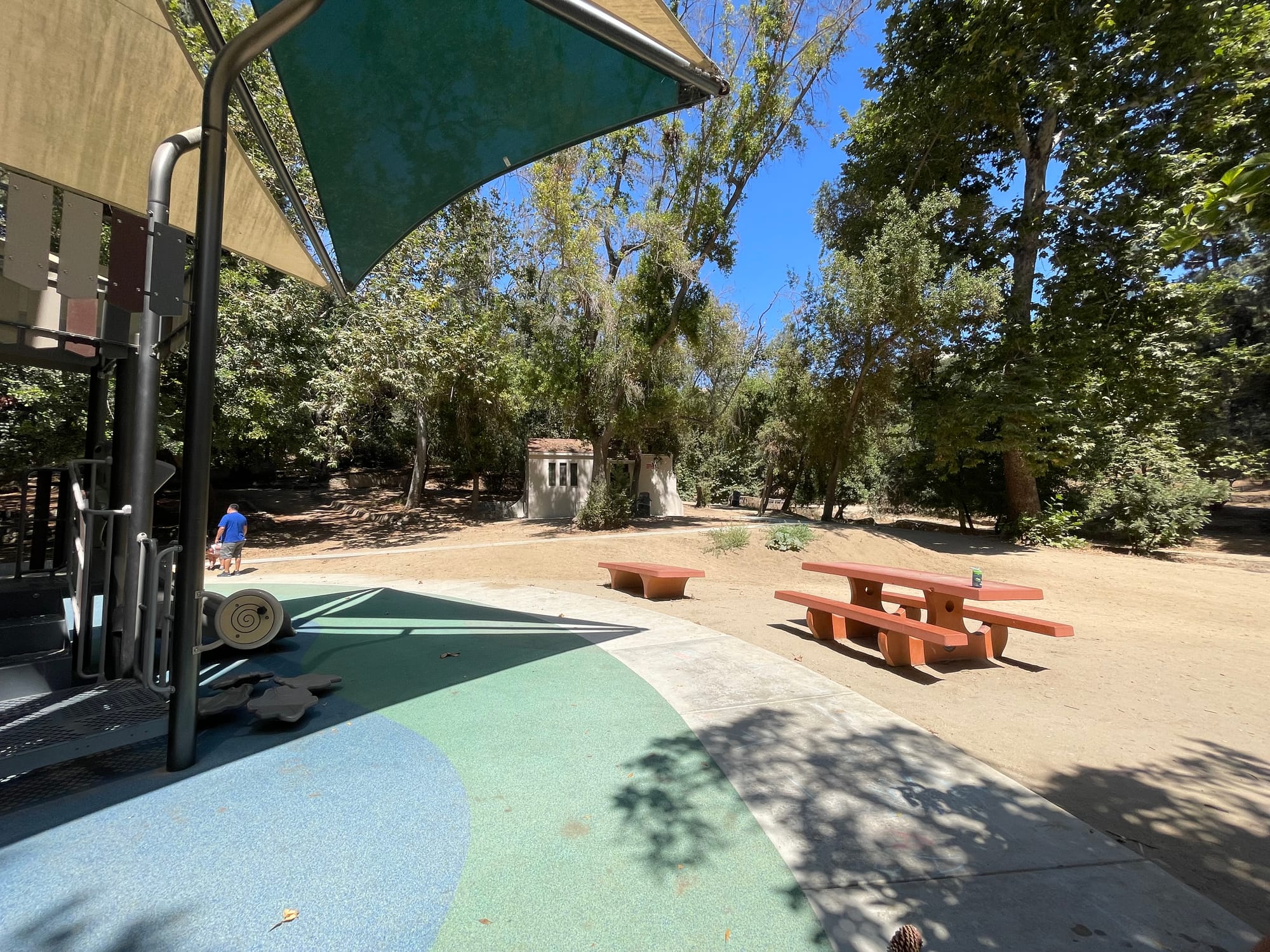 A new playground in Griffith Park with an attractive rubber mat and smooth new pavement, but the bench and picnic table to use at the playground are off to the side installed in the dirt