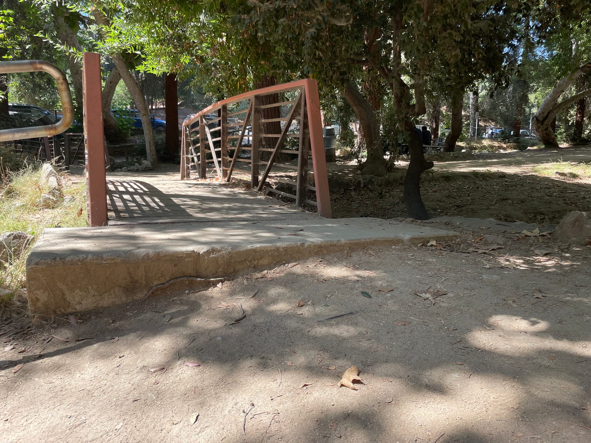 A wooden and steel bridge connects a shady, oak-planted ravine of Griffith Park, but the pavement has completely fallen away on one side, creating a steep dropoff