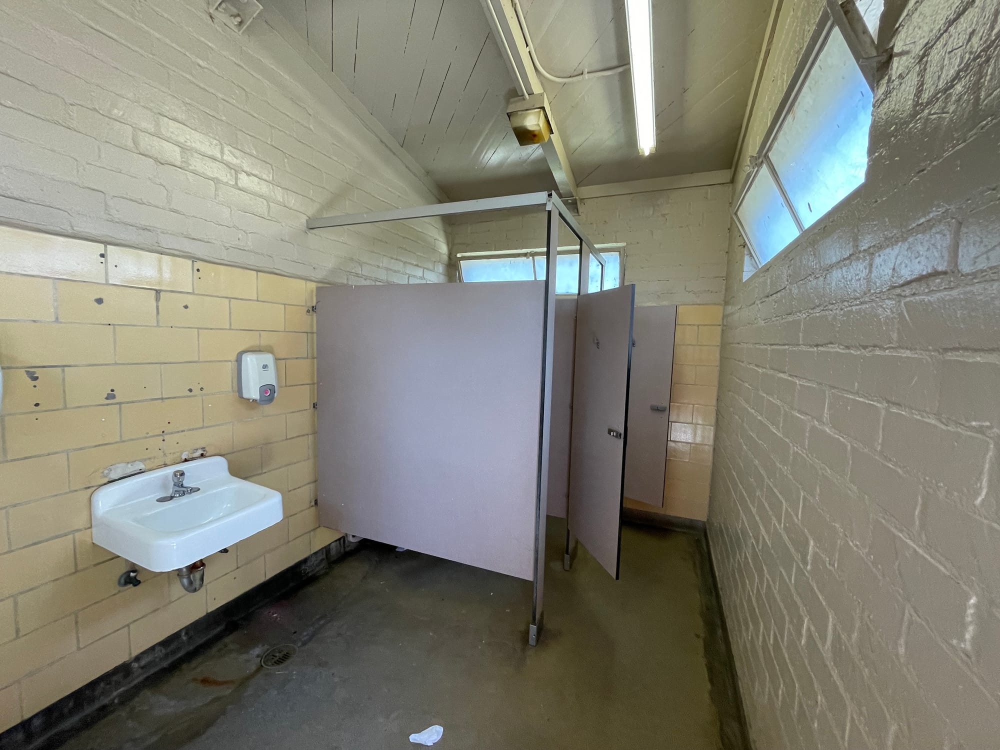 The team building bathrooms at Cheviot Hills have yellow tile walls, a single sink, and two lavender stalls which are very narrow and not ADA compliant