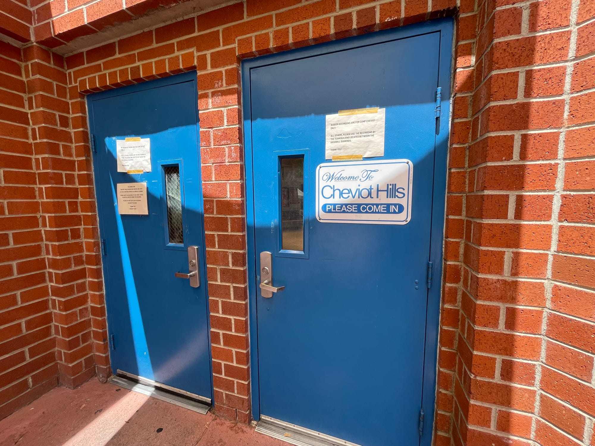 A sign taped to two large blue doors says bathrooms are for campers only and instructs people to use the bathrooms in the team building instead