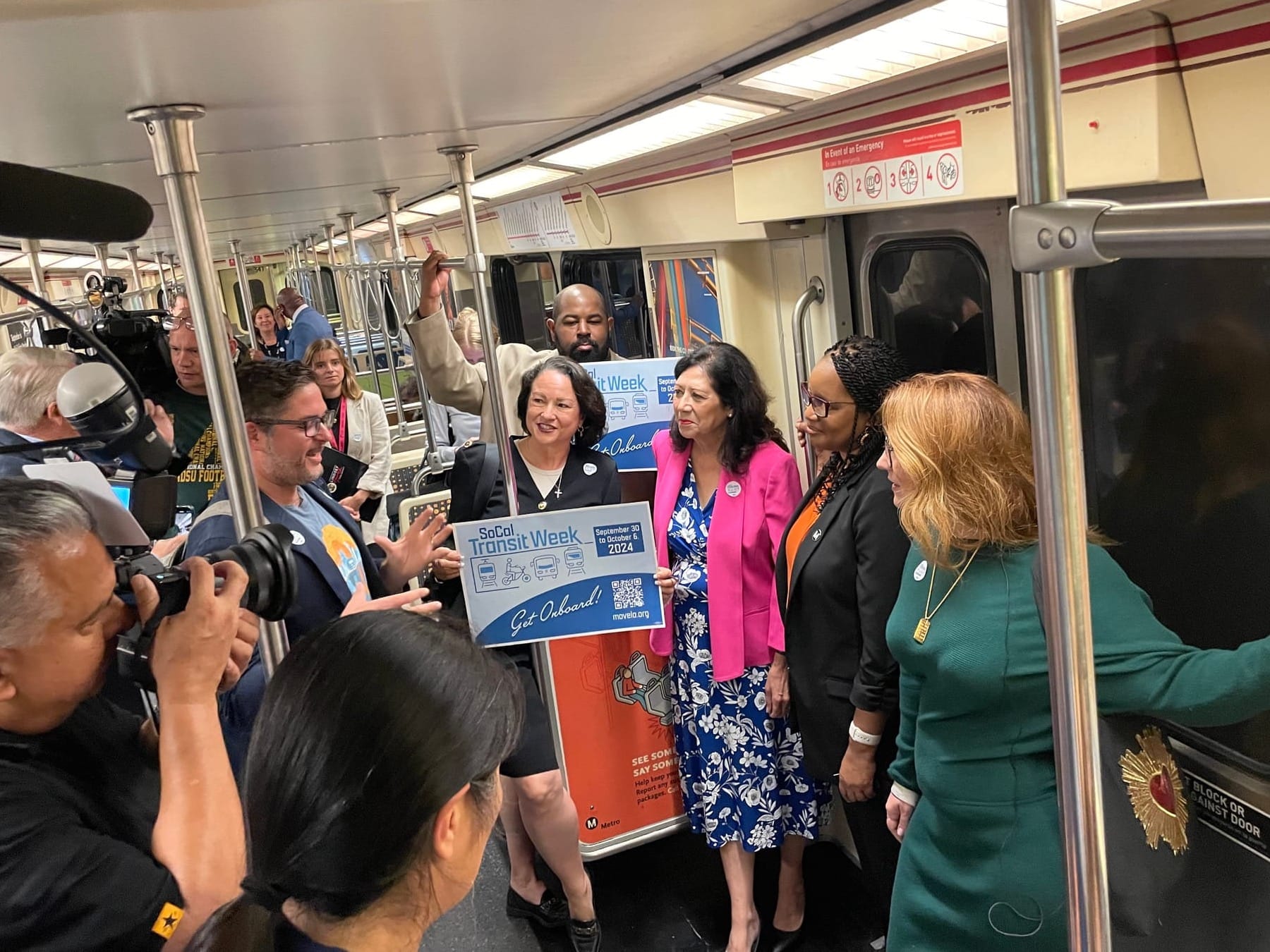 Elected officials riding the subway with a large group of journalists taking photos, a sign reads SoCal Transit Week: Get onboard