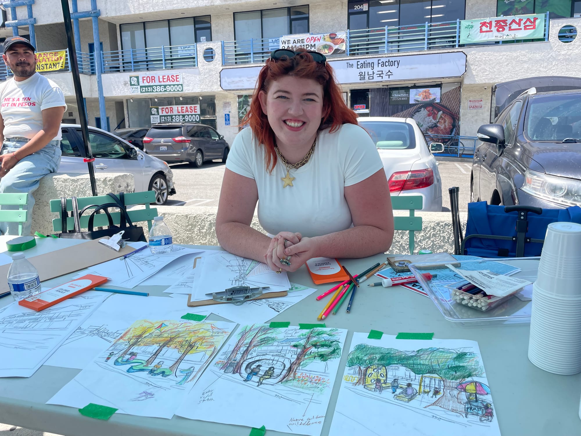 A artist with red hair at a table with colored pencils drawing images of beautiful bus shelters