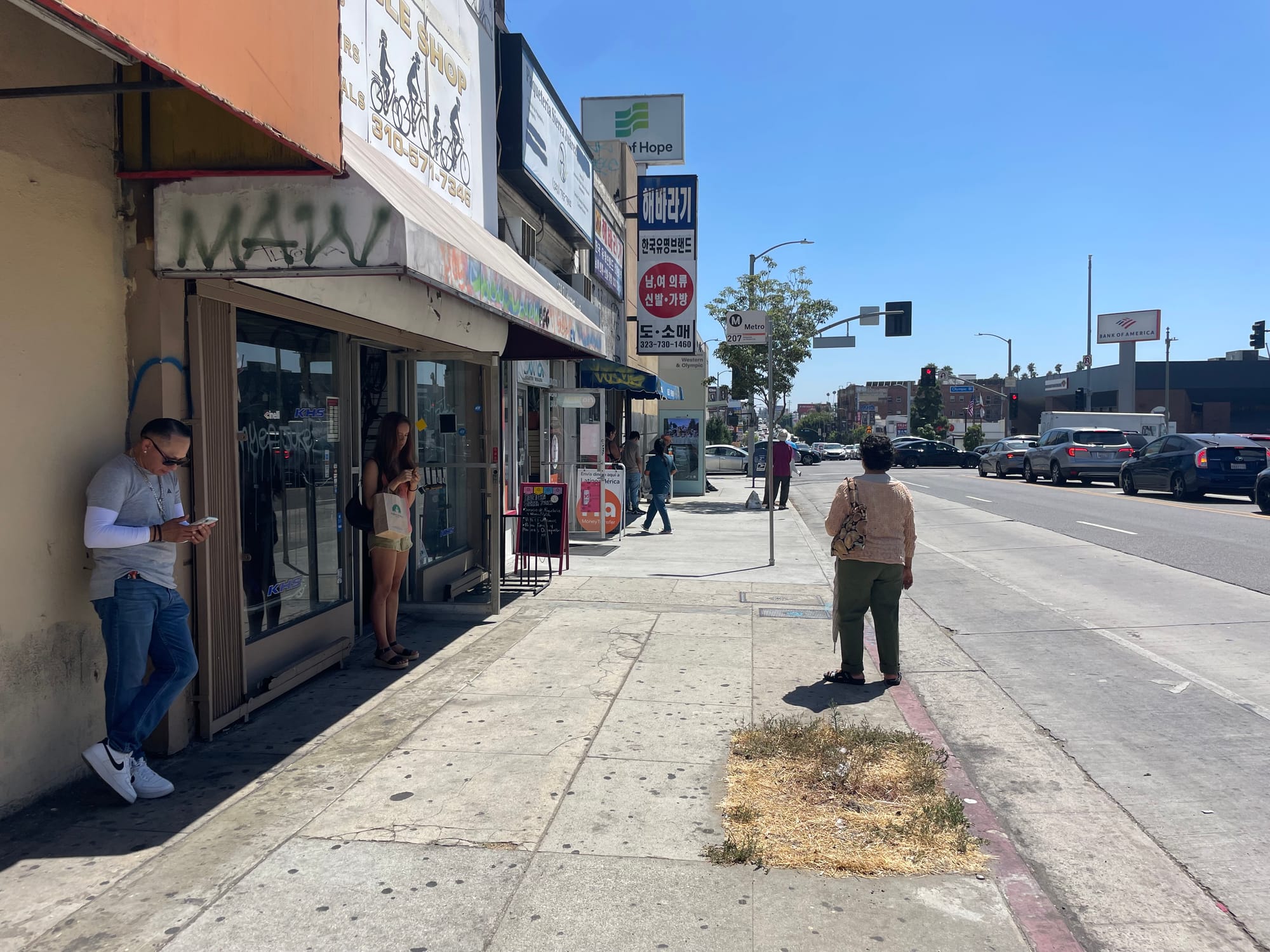 The same bus stop with even more people huddled into the shade as they wait