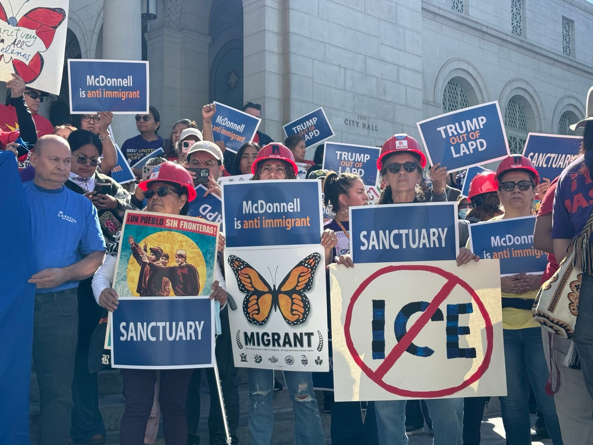 Workers on the steps of City Hall holding signs that say Sanctuary, No ICE, trump out of LAPD, McDonnell is anti immigrant