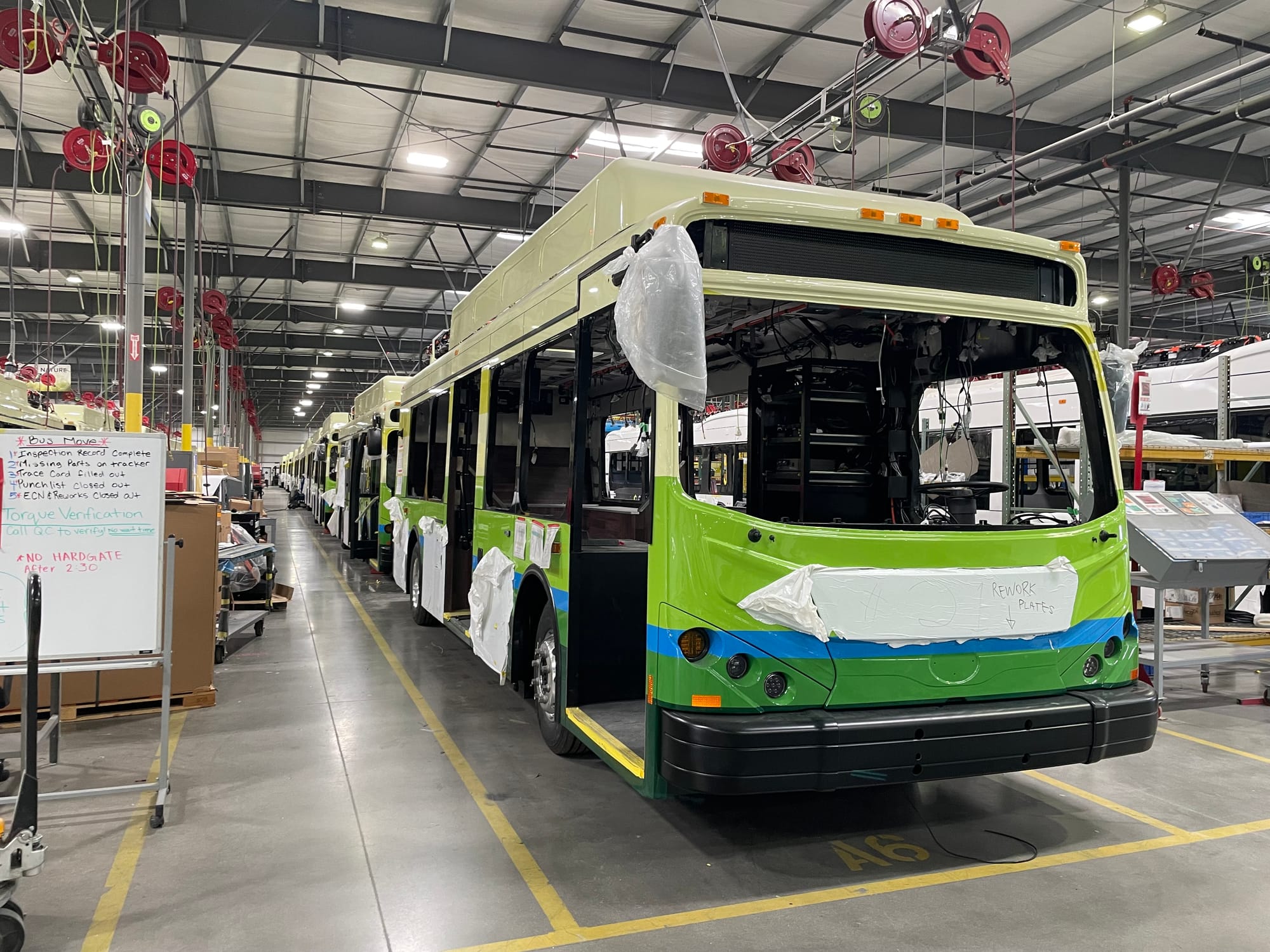 A bright green and blue DASH bus being assembled on a massive factory floor at BYD