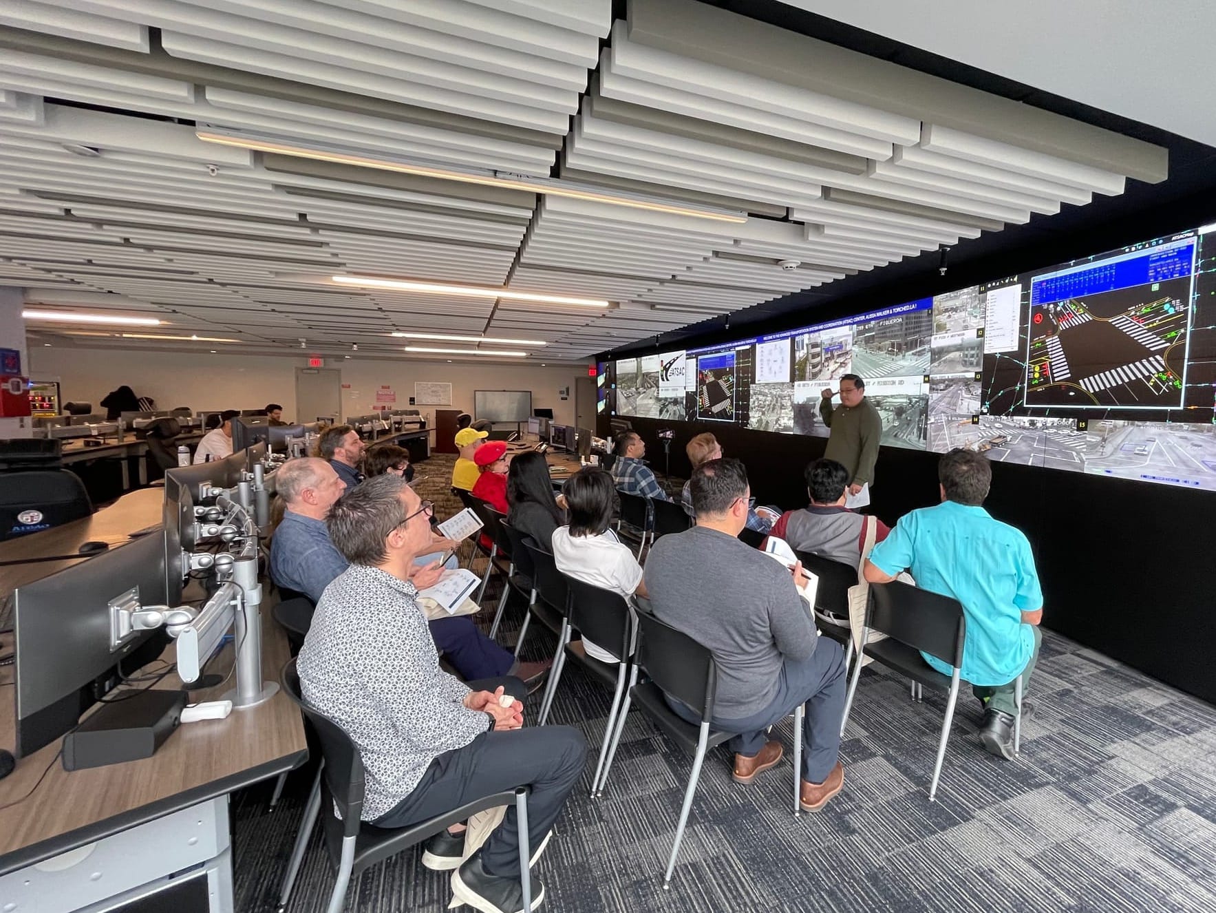 A group in an official-looking room watches attentively while a huge screen showing video feed of LA streets and intersections at the LADOT building