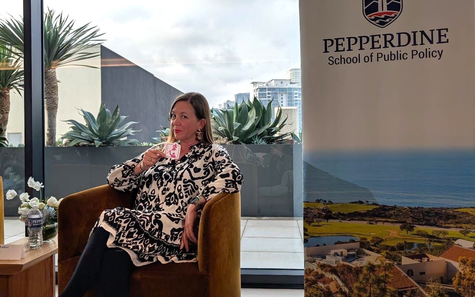 It's me sitting in a cozy chair with the downtown skyline behind me and holding a Torched logo sticker with a Pepperdine banner showing the school's campus to my side